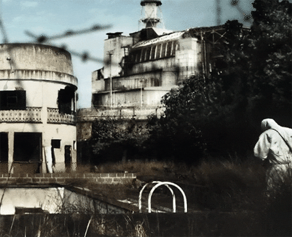 A still from a movie. A person in protective clothing is walking in atomic nuclear plants area where all buildings are destroyed.